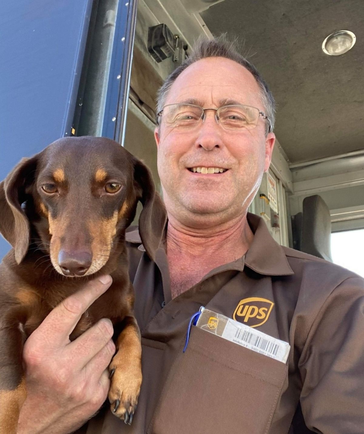 male ups driver holding a brown dachshund in his arms