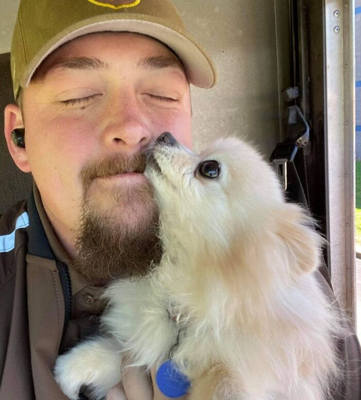male ups driver in the truck getting licked in the face by a small fluffy white dog