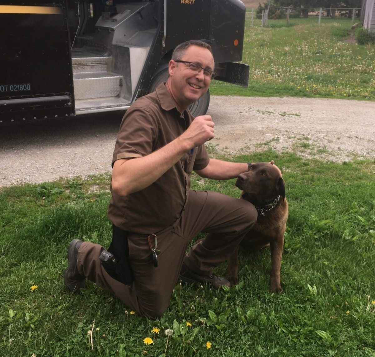 male ups driver kneeling on grass petting a brown dog