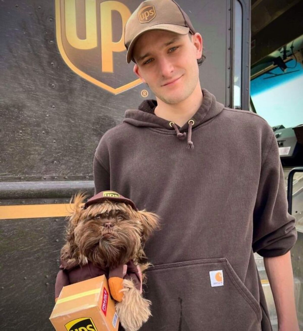 male ups driver standing and holding a brown fluffy dog in a ups driver uniform