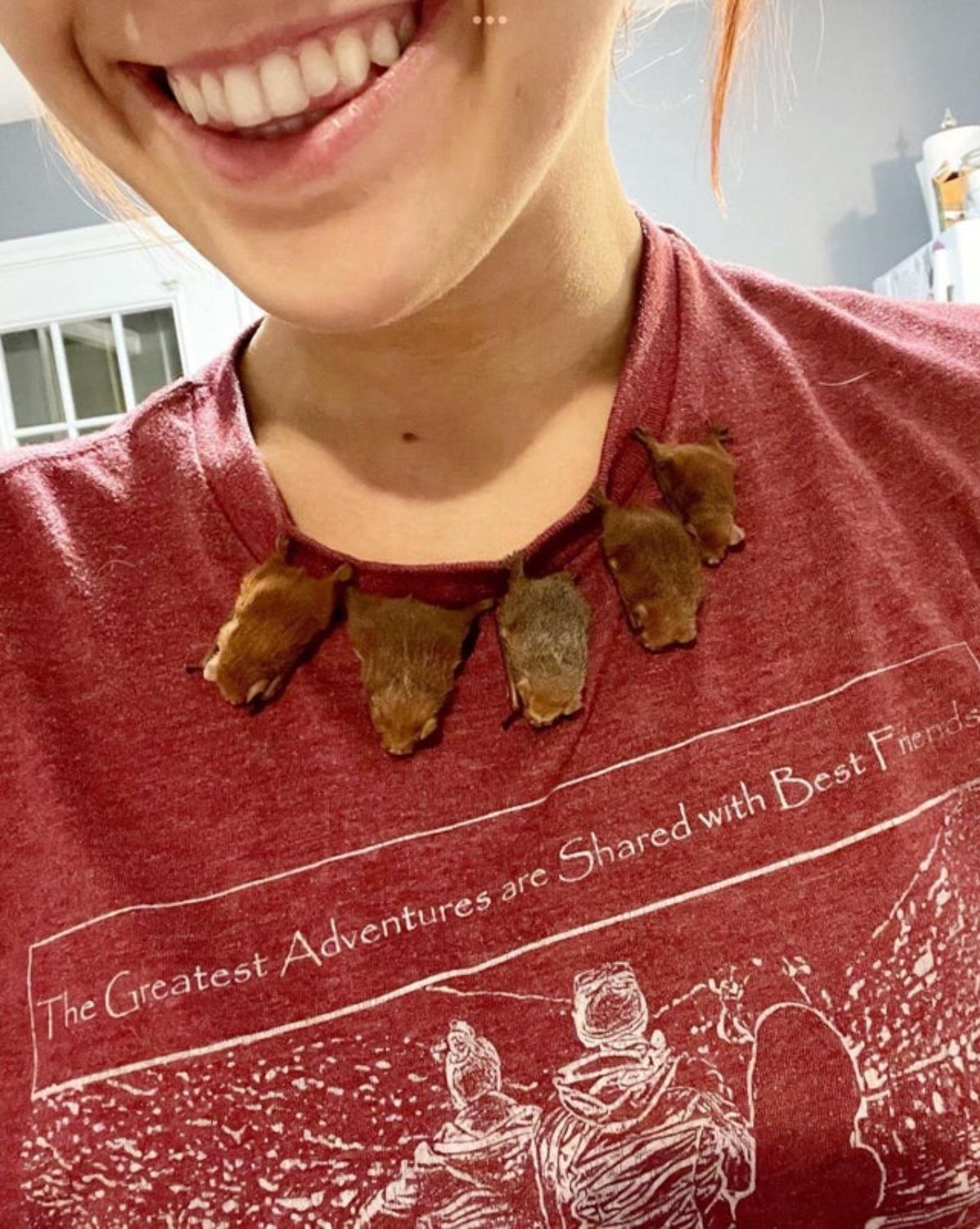 5 small bats hanging off of the collar of a red t shirt worn by a woman