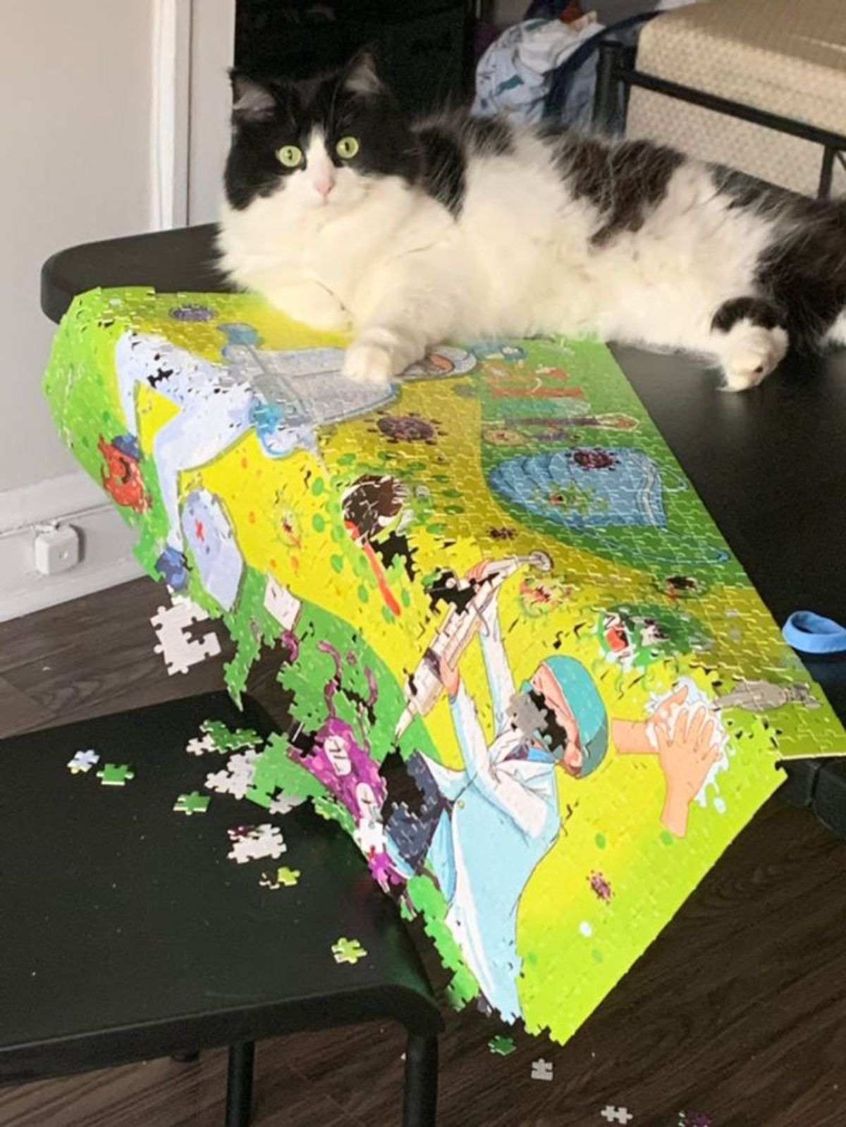black and white fluffy cat laying on a table and pushing a mostly completed puzzle off of it