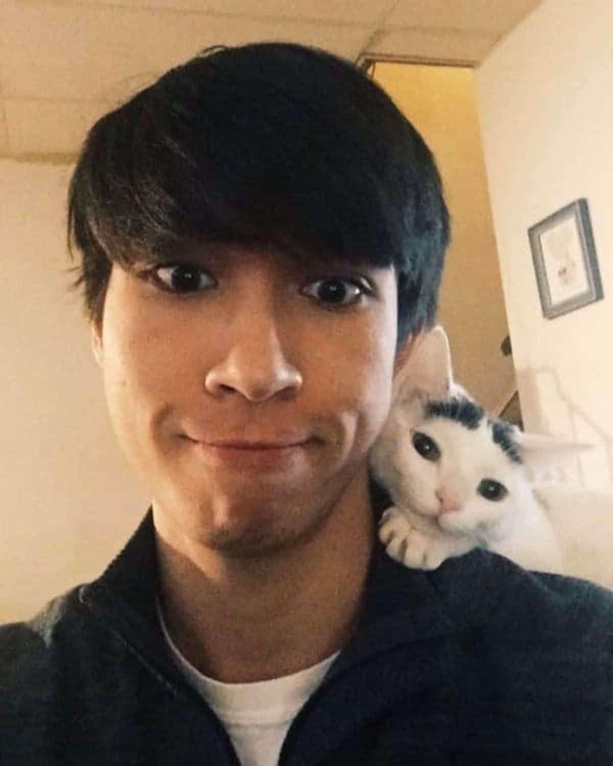 black and white kitten peeking from behind a man