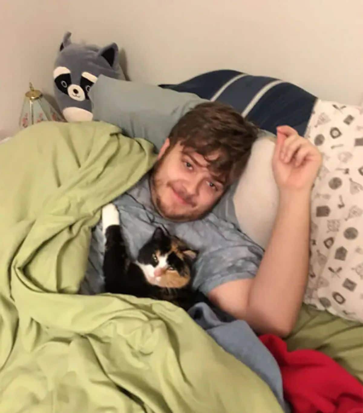 black white and orange cat laying in a bed with a man under a green blanket