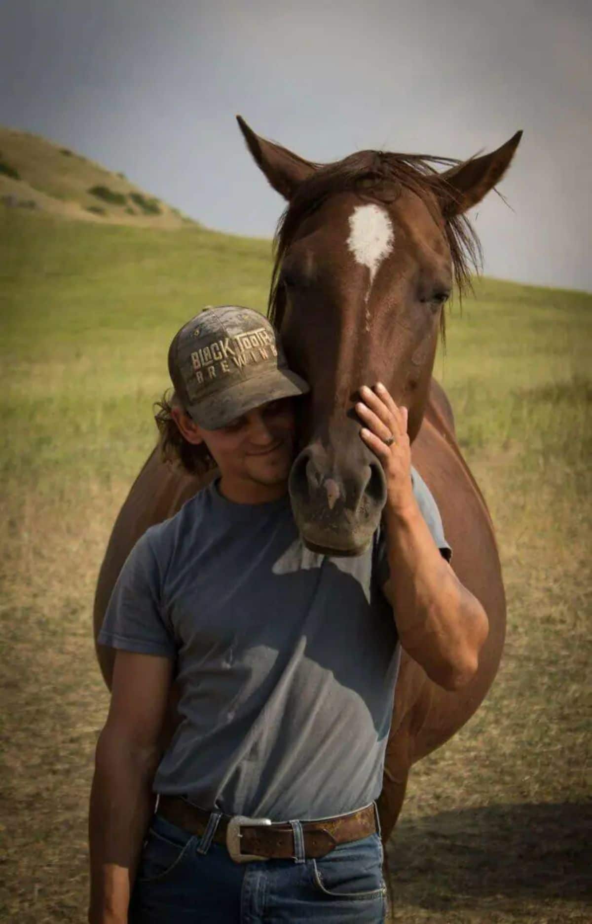 brown horse nuzzling a man wearing a cap