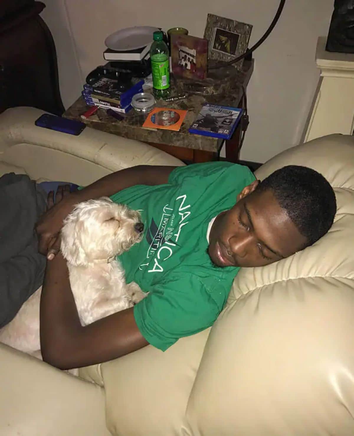 white fluffy dog sleeping cuddled up with a man wearing a green t shirt on a beige chair