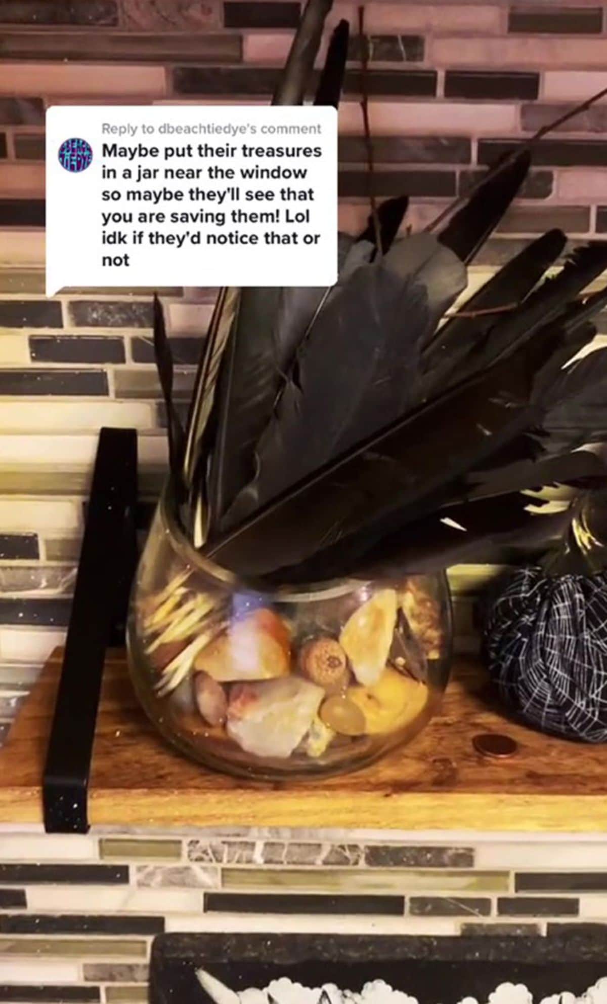 a jar of black feathers and other assorted things in a glass jar on a table