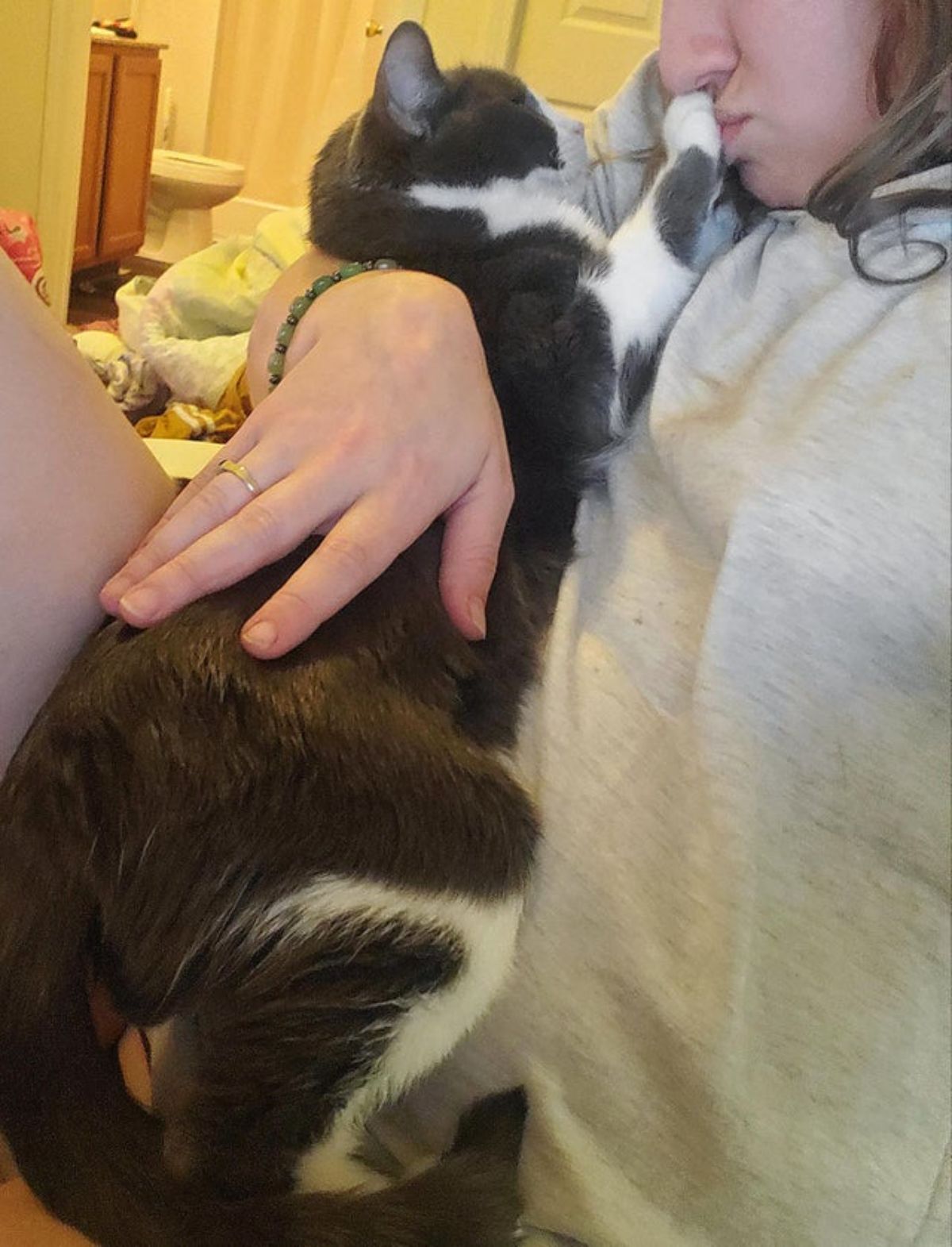 black and white cat getting hugged by a woman and the cat is placing a paw on the person's mouth