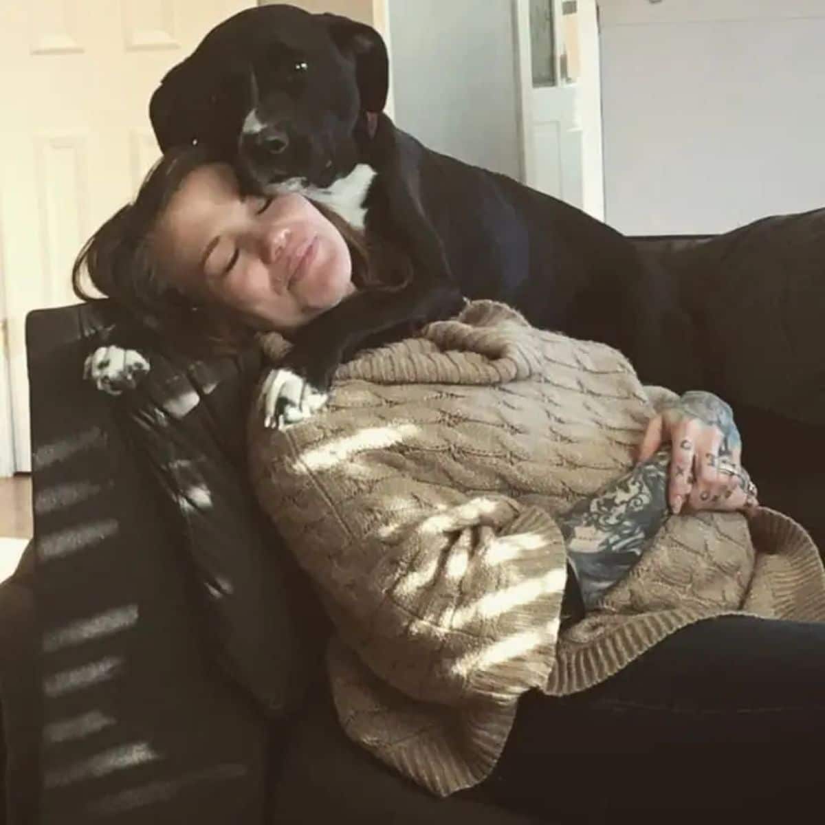 black and white dog hugging and laying on a woman laying on a brown sofa