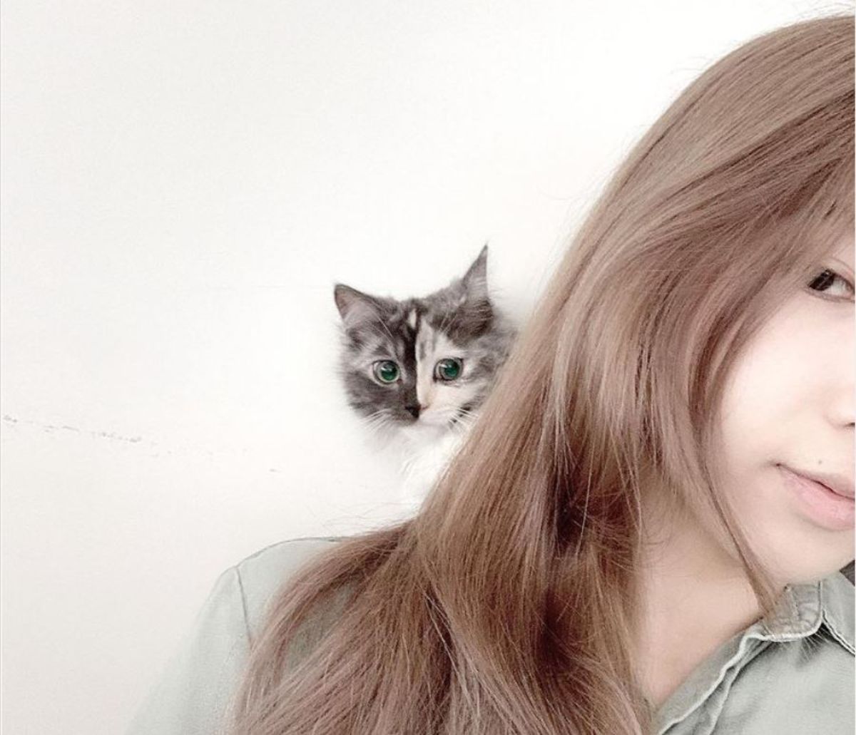 fluffy kitten with right side of face being grey and left side being black on a woman's shoulder and peeking from behind her hair