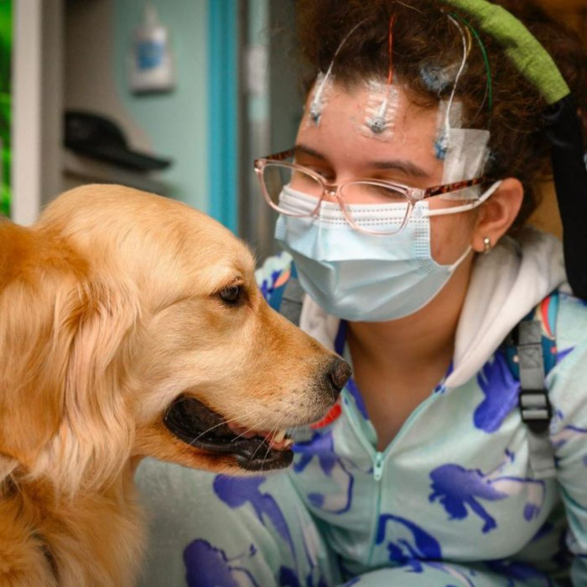 girl with electrodes in her head crocuhing down next to a golden retriever