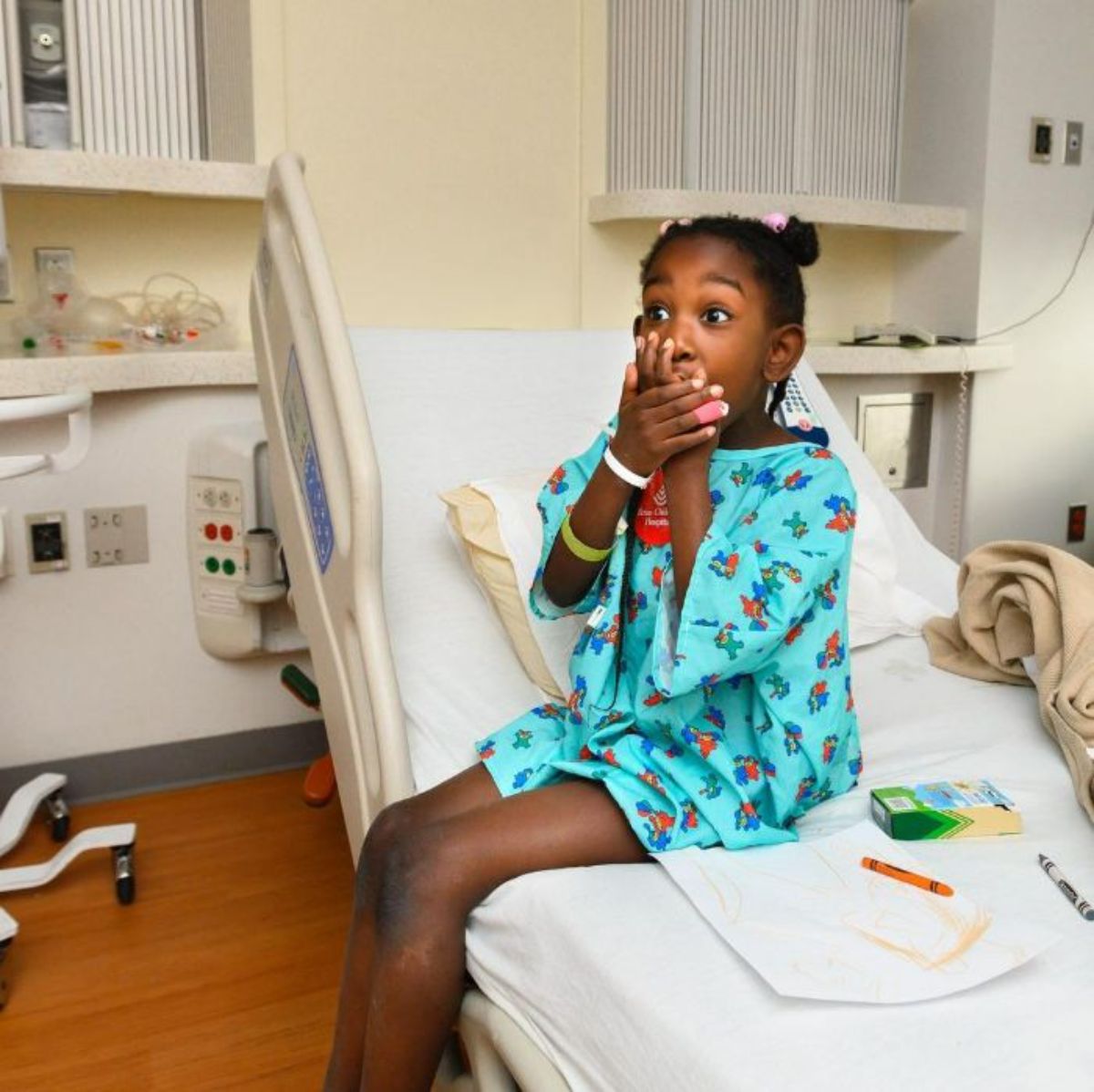 little african american girl sitting on a hospital bed holding both palms to her mouth