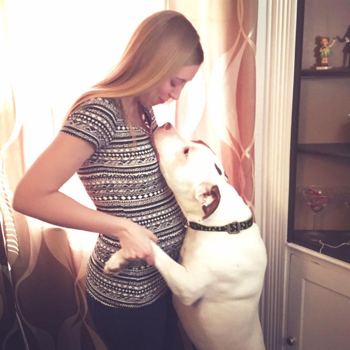 white dog standing on hind legs leaning against a pregnant person and having the front legs held by a pregnant person