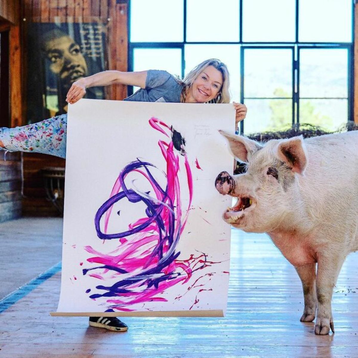 white pig standing next to a woman holding a white canvas with pink and purple paint