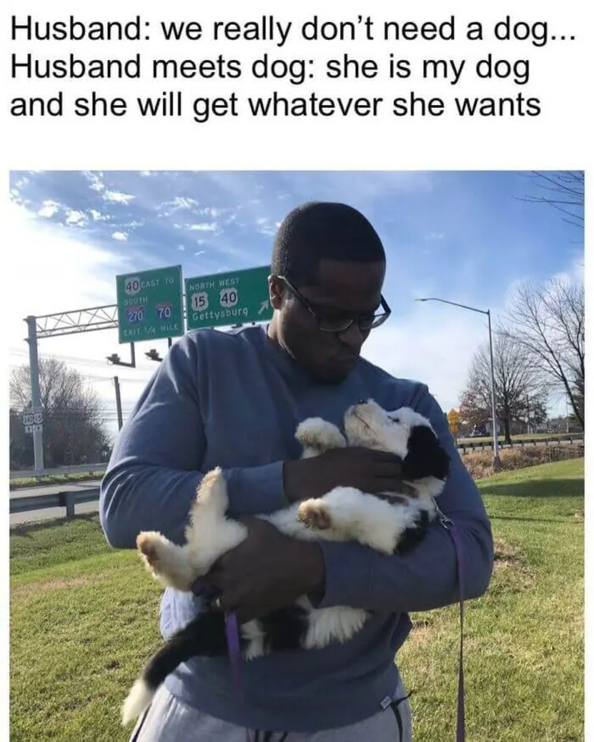 man holding a black and white dog like a baby with caption saying the husband didn't want the dog but now loves the dog