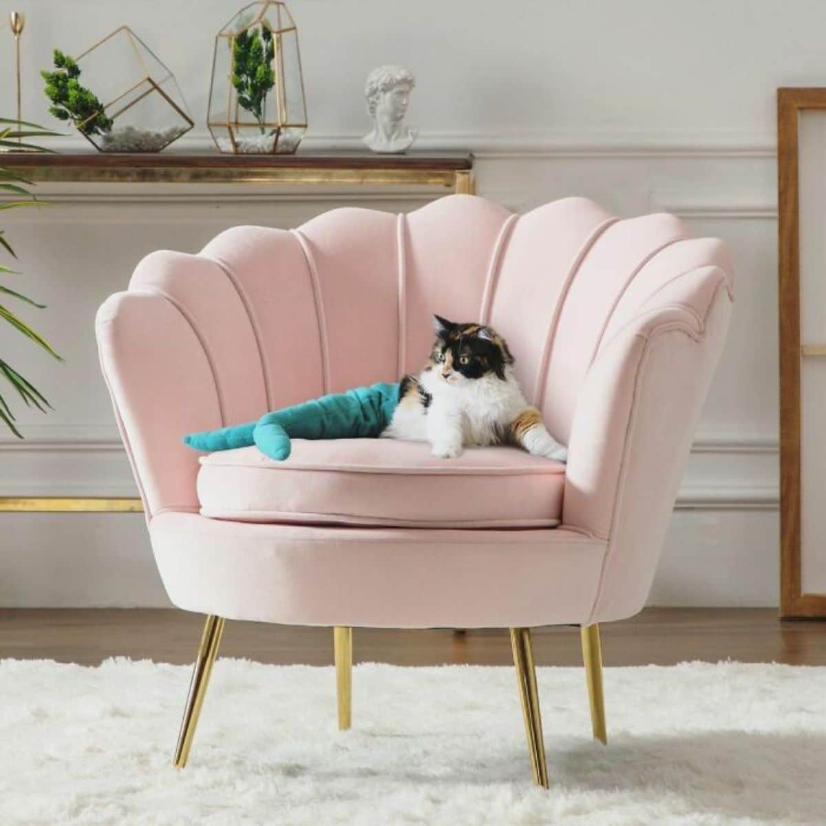 white black and orange cat wearing a blue mermaid tail laying on a pastel pink seashell chair