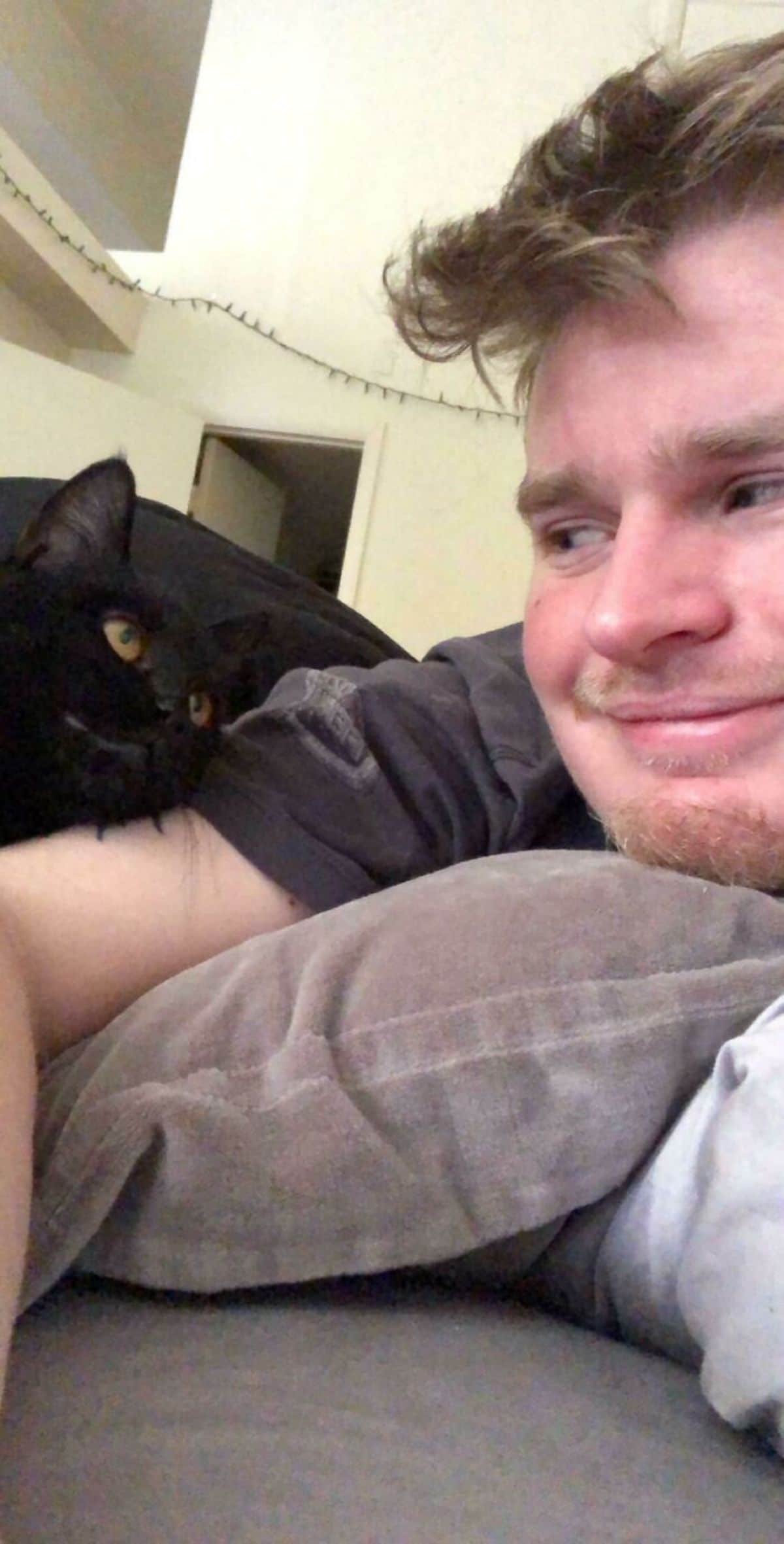black cat looking lovingly at a man laying on a bed