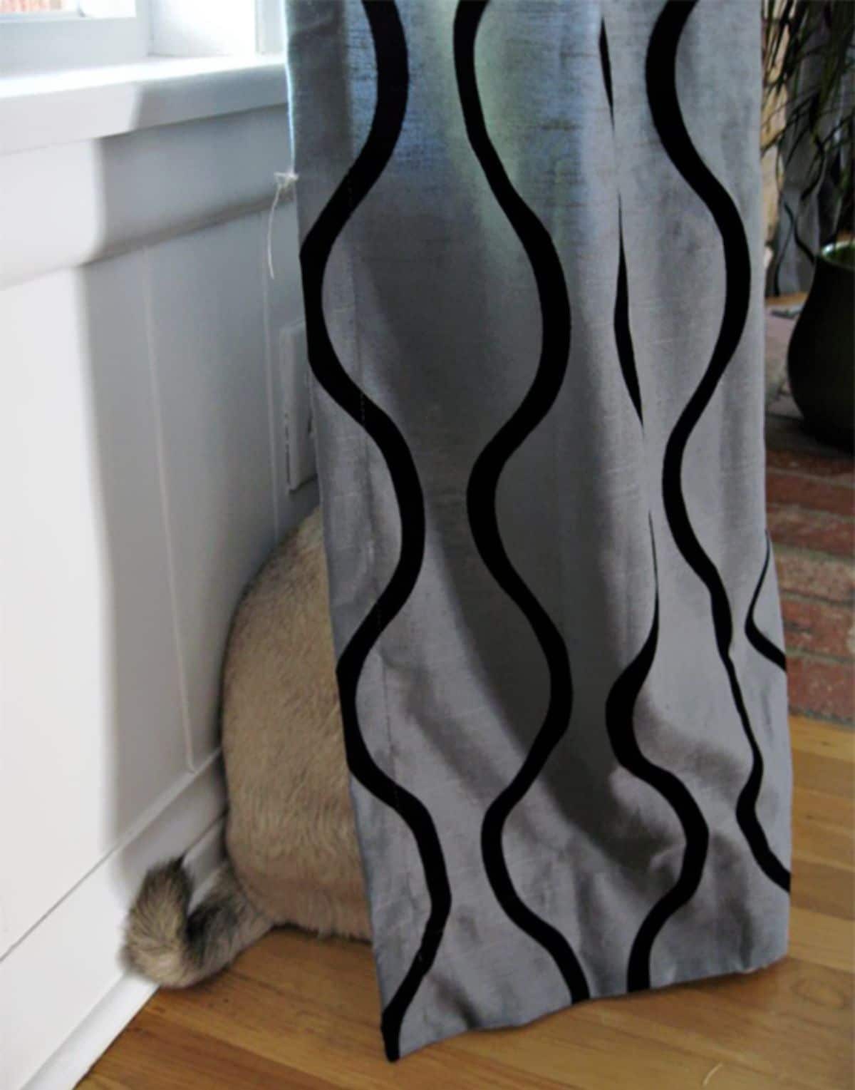 brown and black dog hiding behind a silver and black curtain with the back and the tail showing