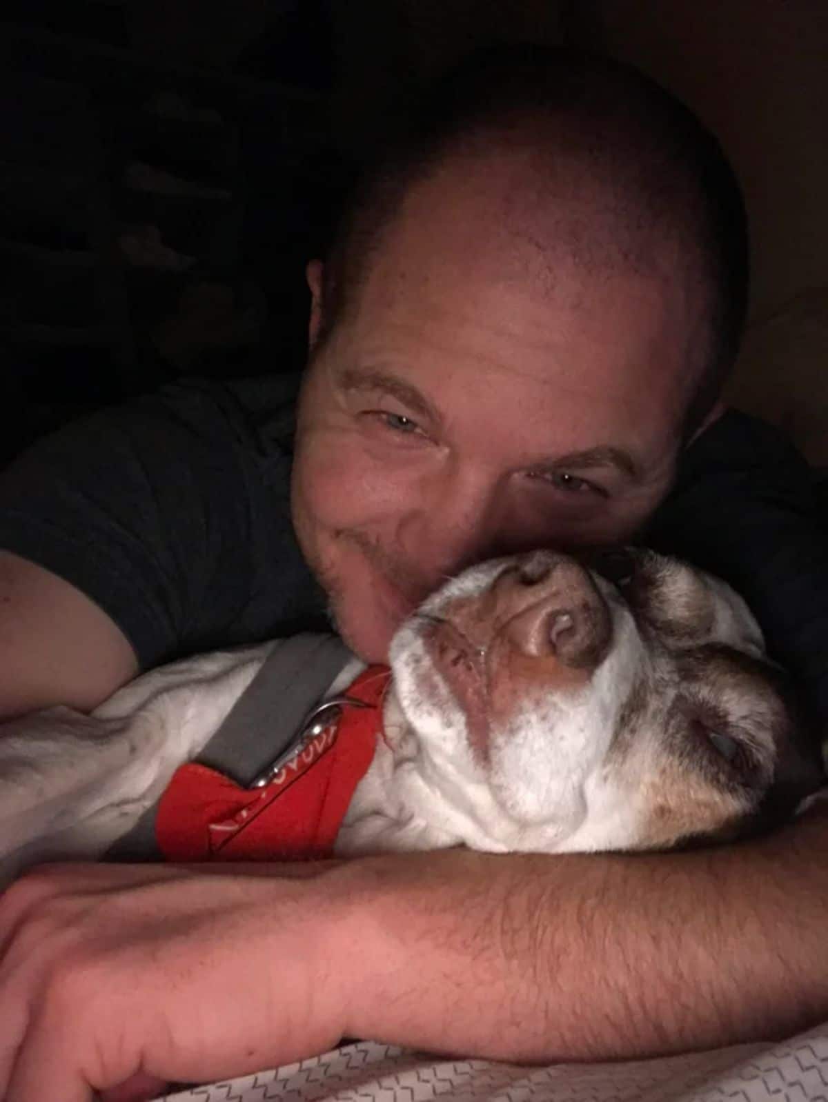 man cuddling with a white black and brown dog