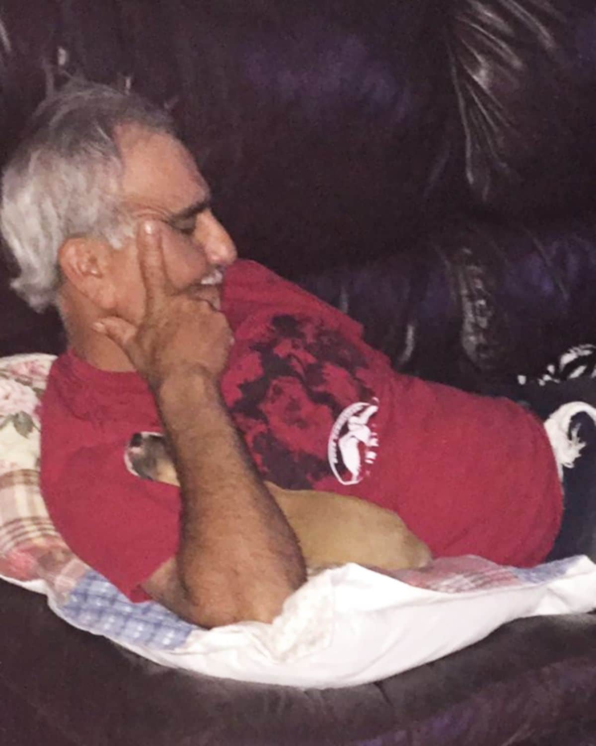 brown puppy sleeping under an old man's arm