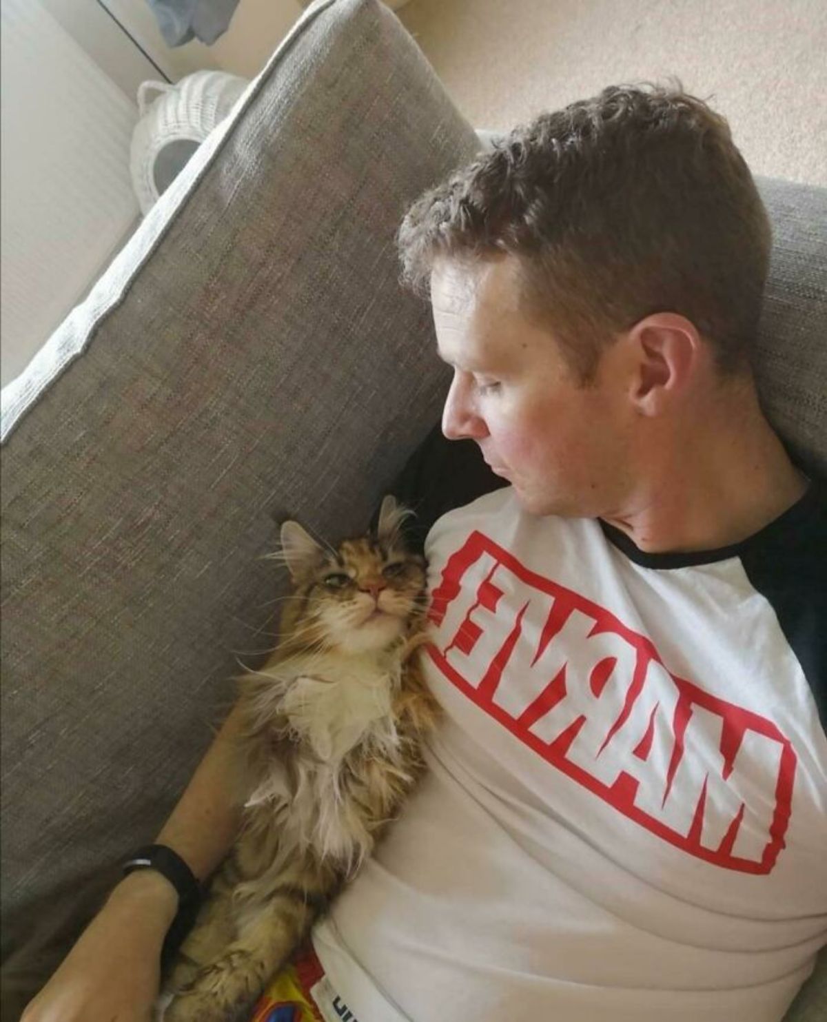 fluffy white orange and black cat laying belly up next to a man on a brown sofa and they are looking at each other lovingly