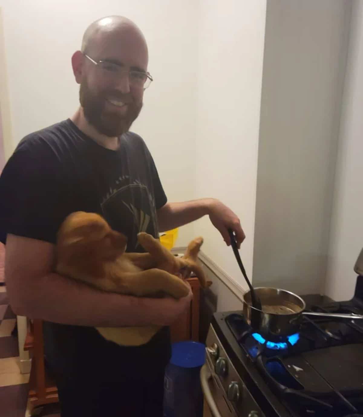 man cooking something on a stove while holding a golden retriever puppy