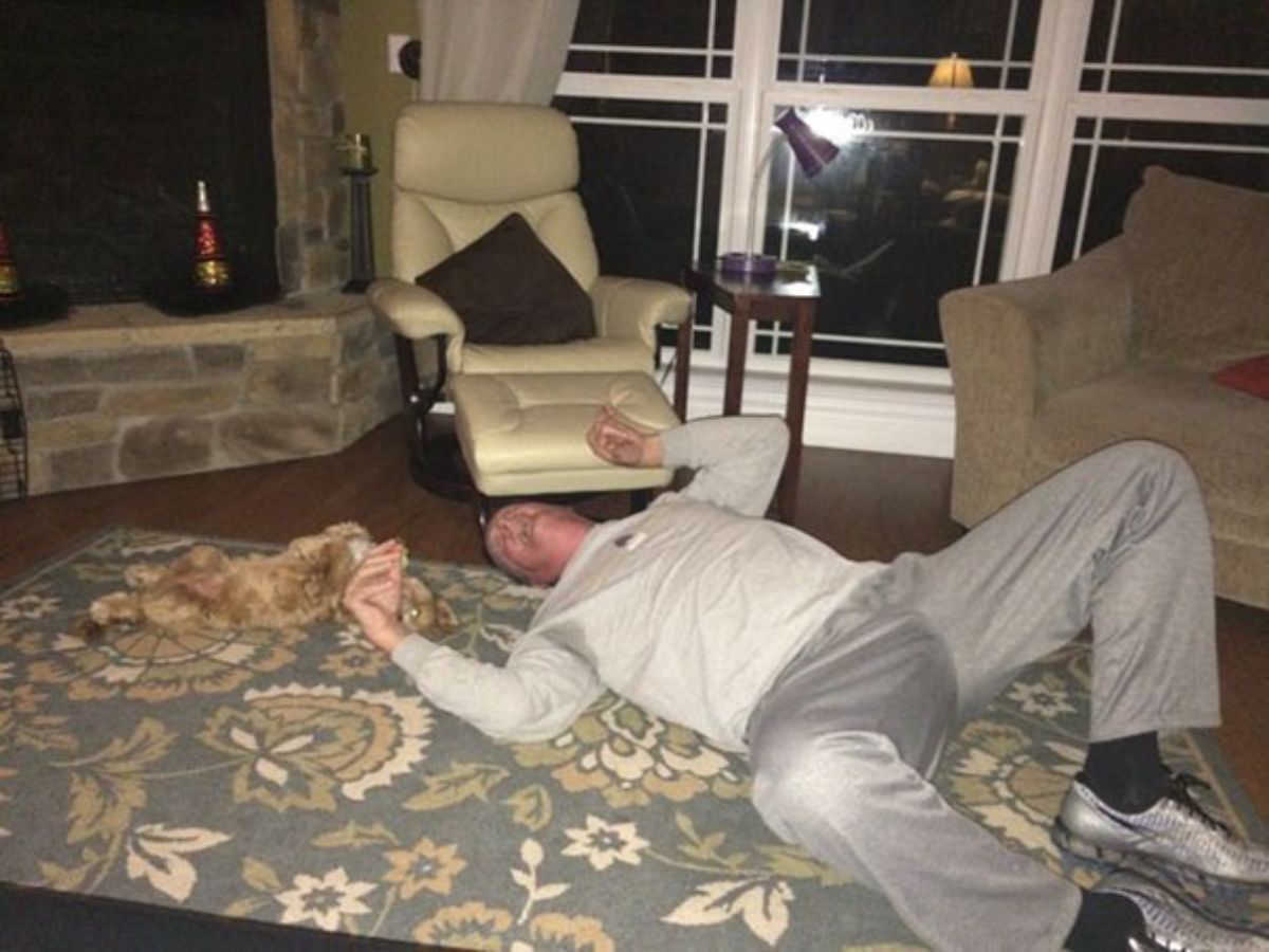 man laying on a rug next to a brown dog