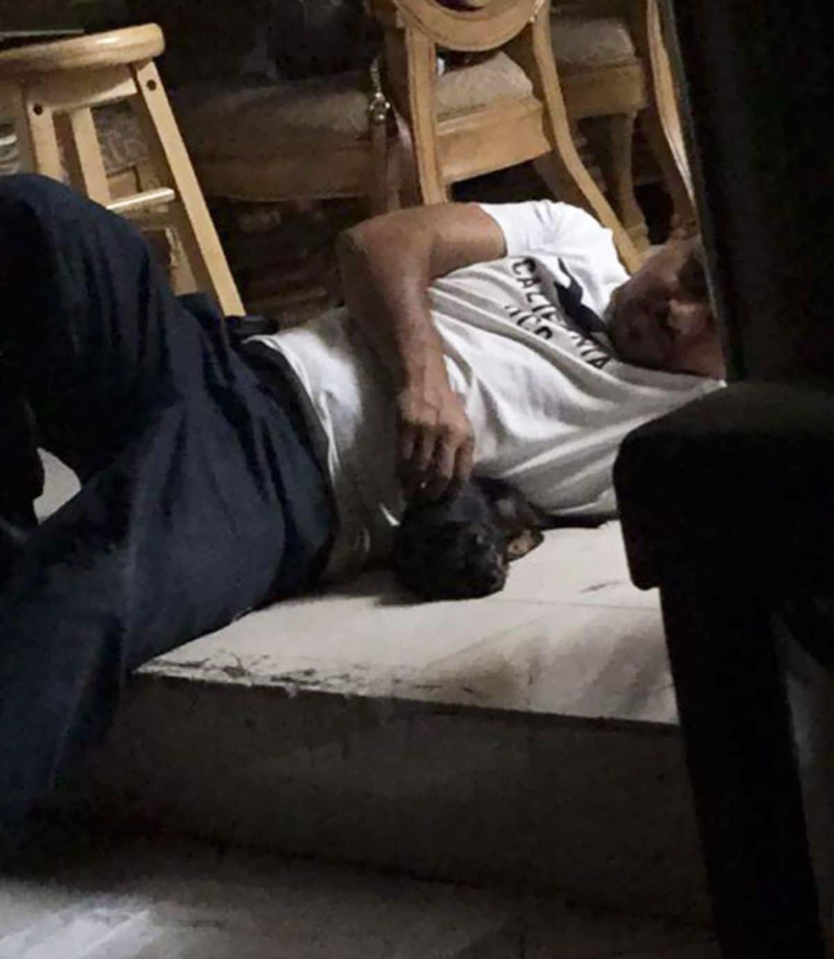 man laying on floor petting a black puppy