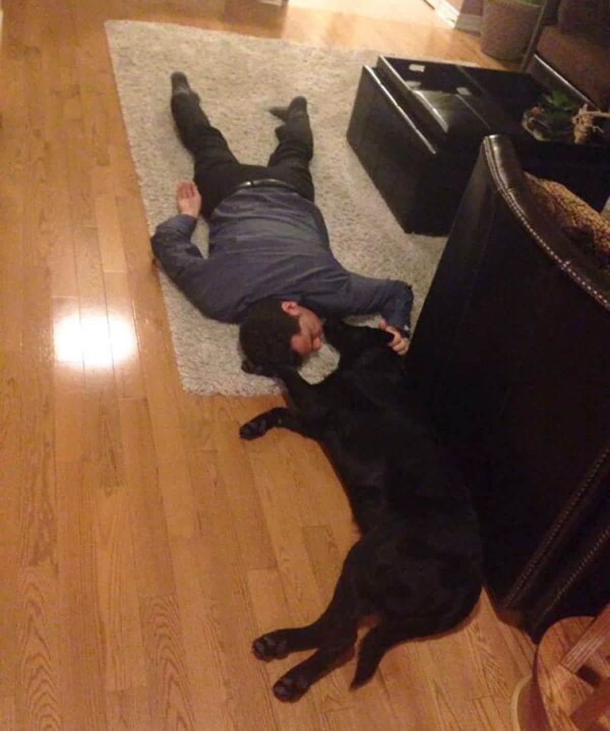 man laying on the floor next to a black dog laying on the floor