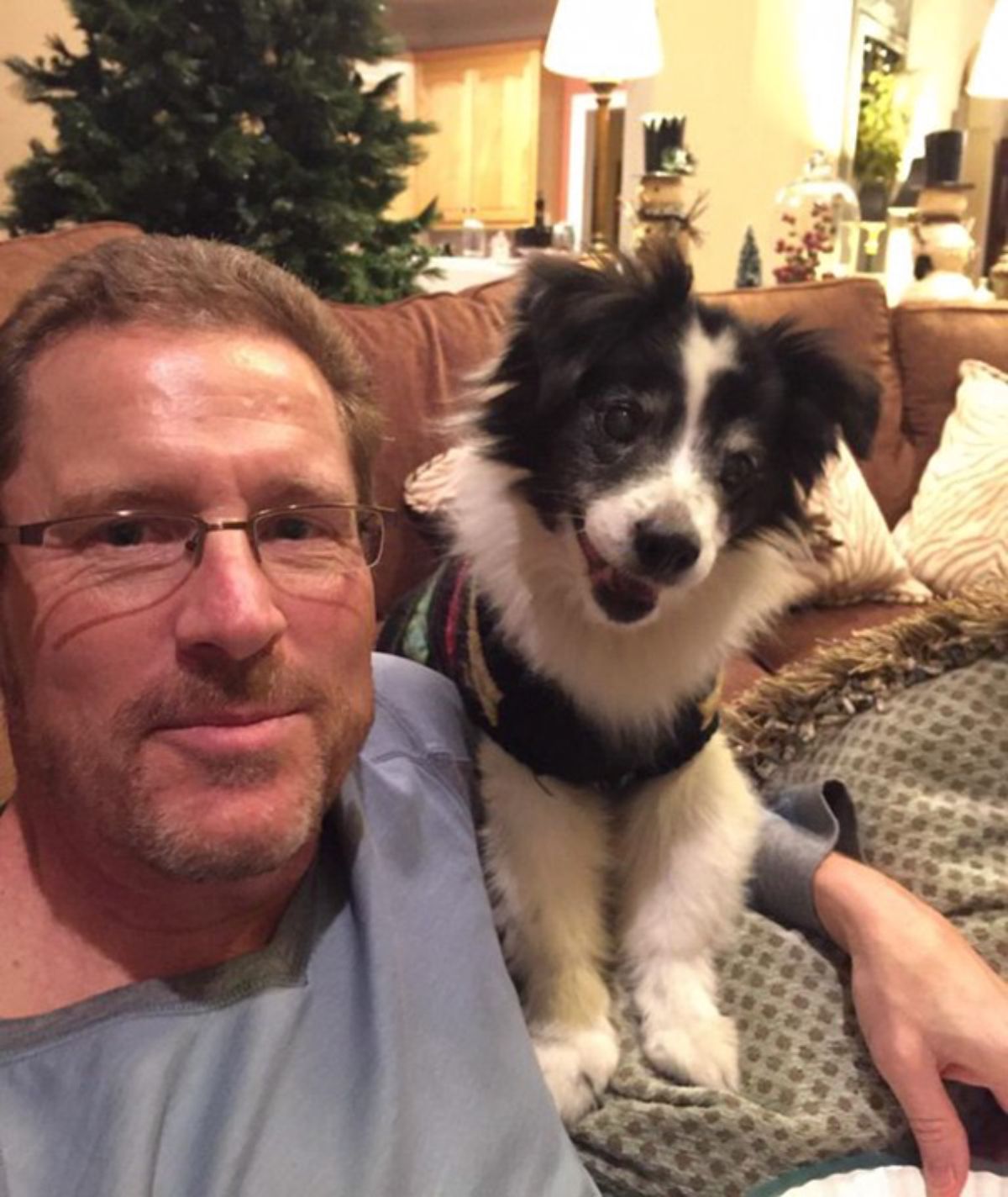 man posing with a smiling fluffy black and white puppy in a black shirt