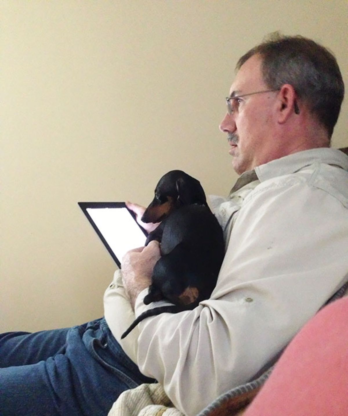 man reading an ebook reader with a black and brown dog on the lap