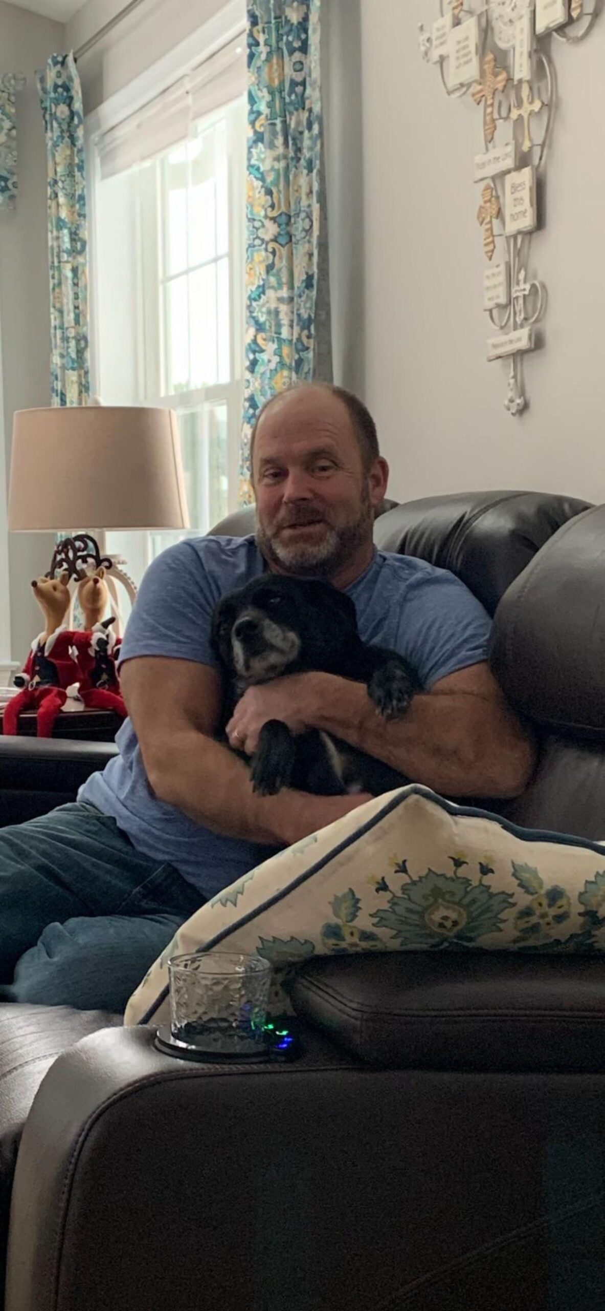 man sitting on black sofa cuddling an old black dog