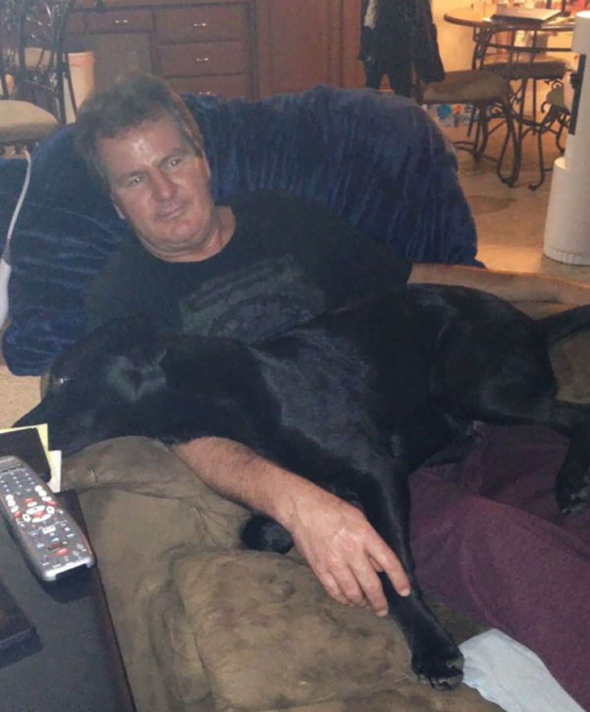 man sitting on chair with a black dog laying on his lap