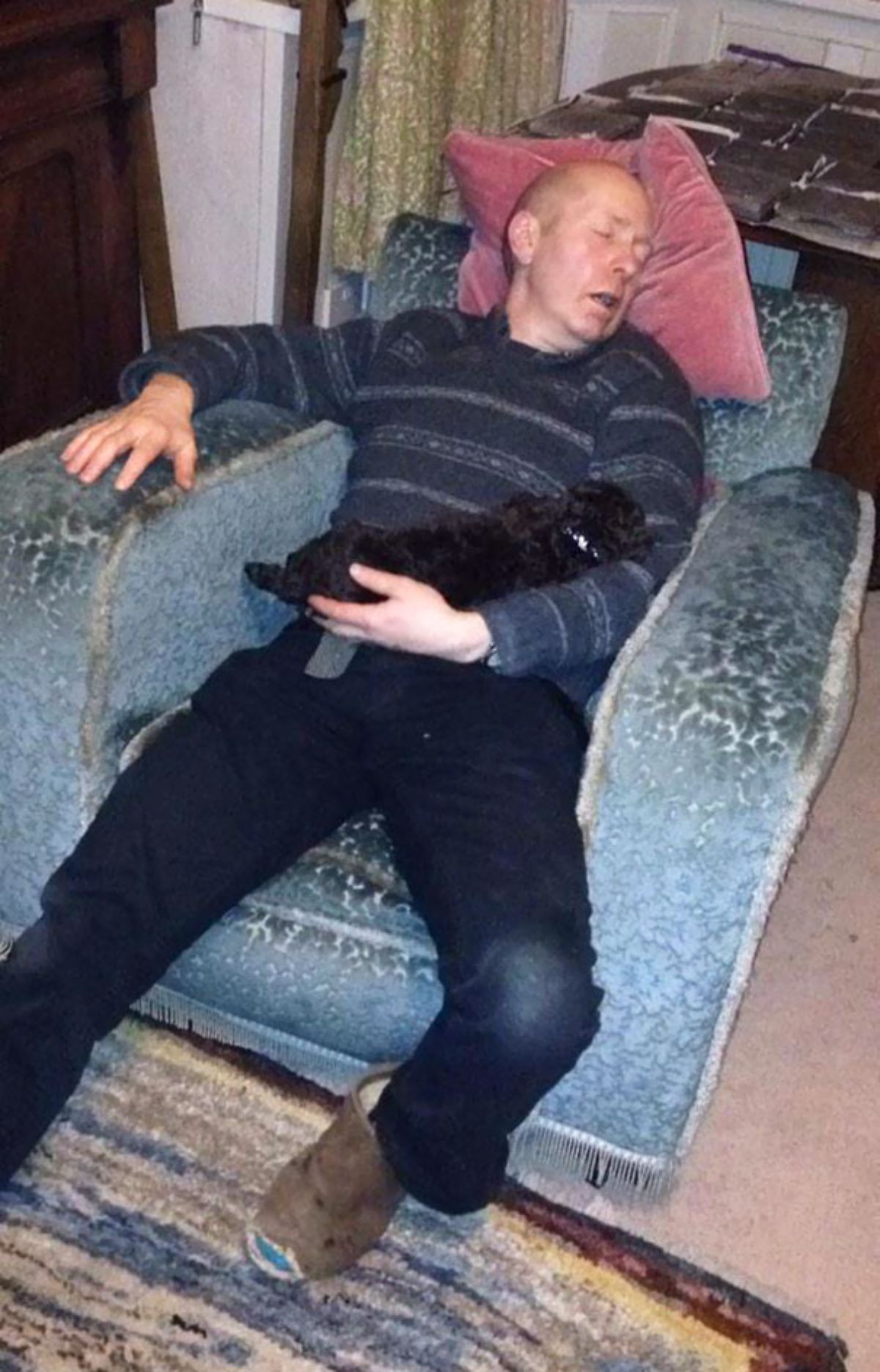 man sleeping on blue chair holding a black puppy
