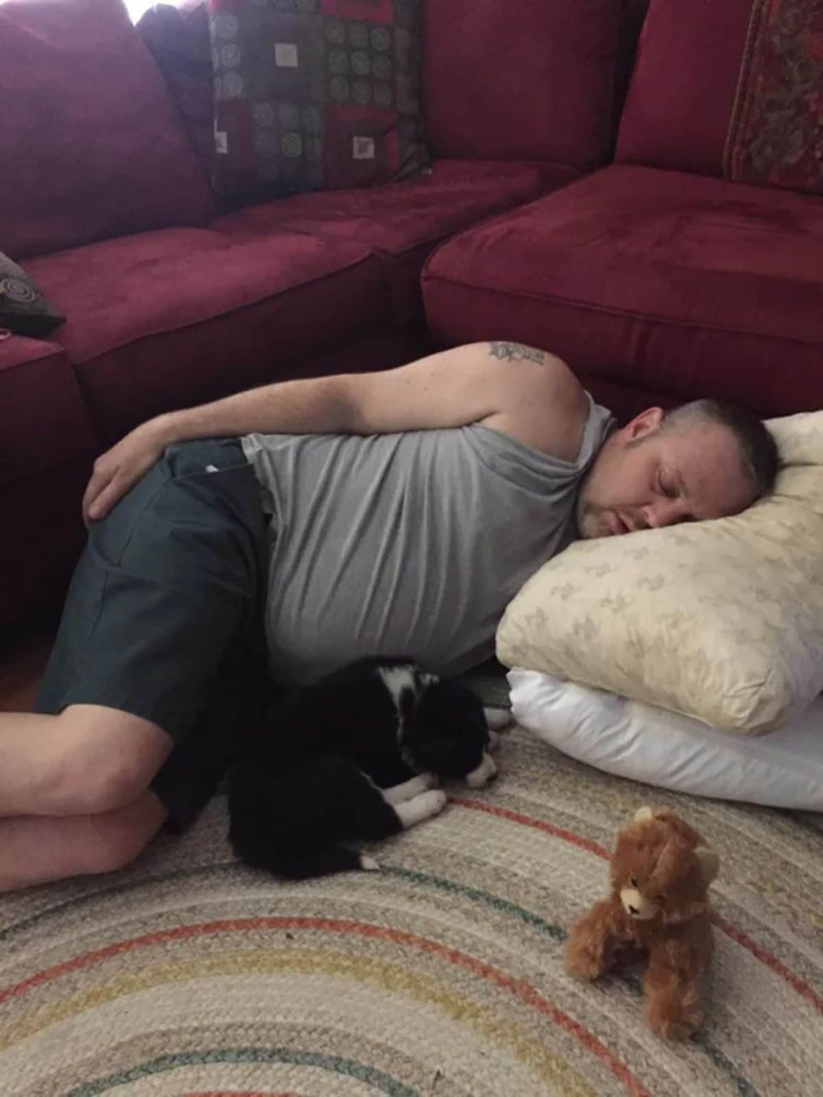 man sleeping on the floor with some pillows next to a black and white puppy