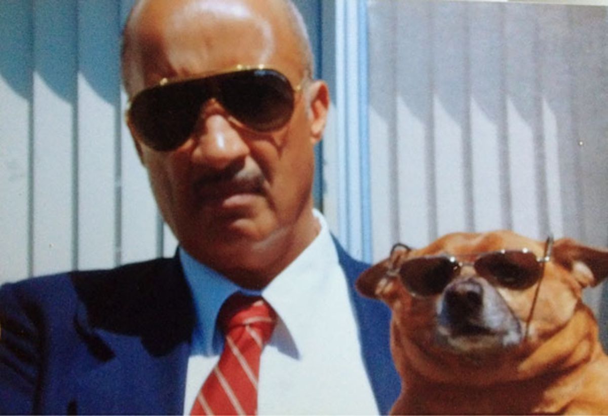 old man in black sunglasses holding a brown and white dog wearing black sunglasses