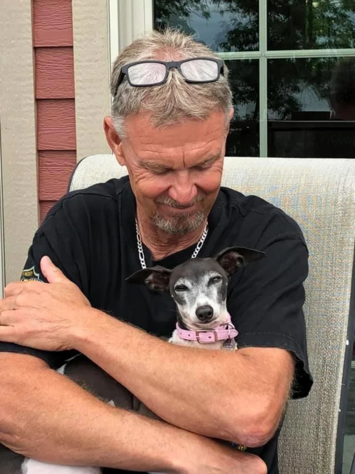 old man sitting and cuddling a black and white small dog on his lap