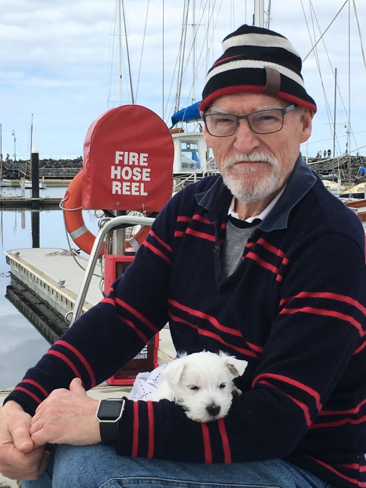 small fluffy white puppy being held by an old man by a boat