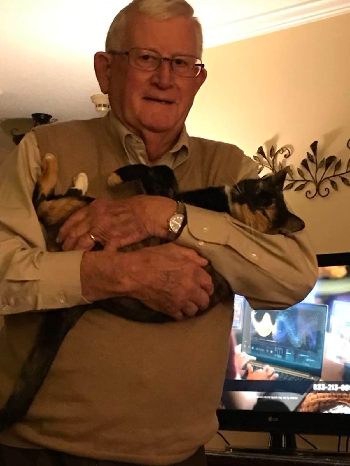 white black and orange cat being held like a baby by an old man