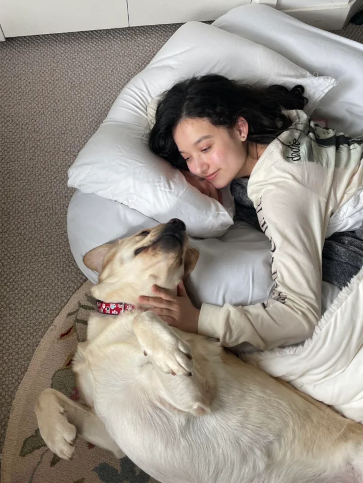 white dog laying belly up on dog bed and looking up at a woman lovingly
