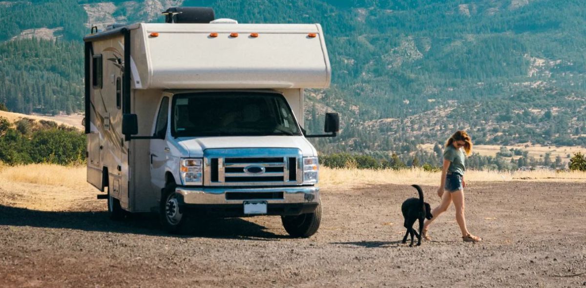 black dog walking next to a woman with a white RV behind them