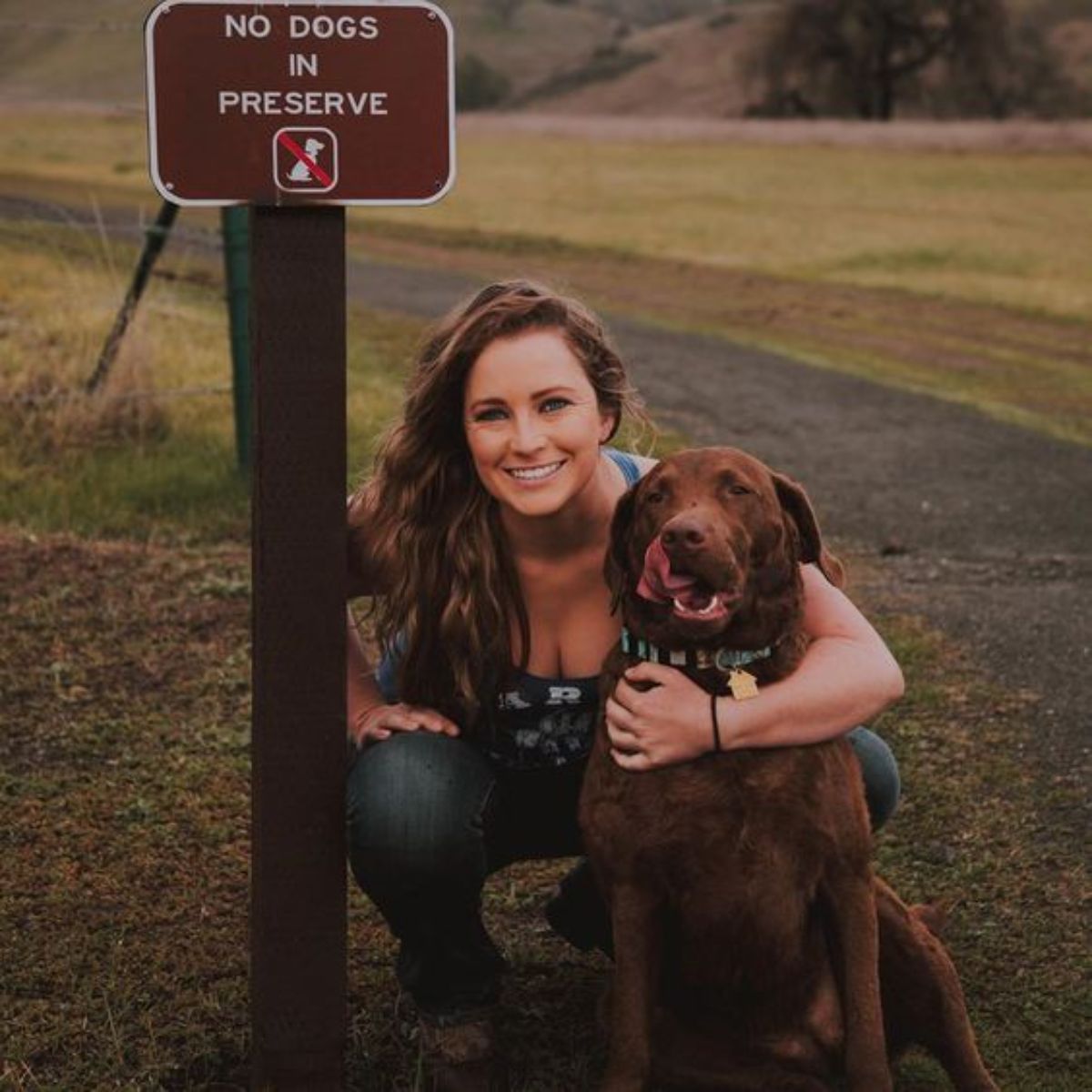 brown dog being hugged by a woman by a NO DOGS IN PRESERVE sign
