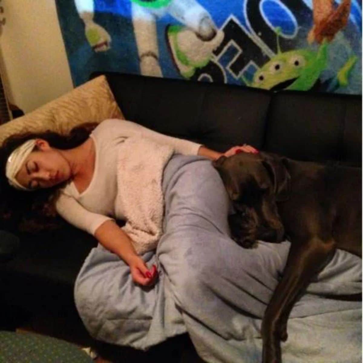 large black dog sleeping against a sleeping woman on a black sofa