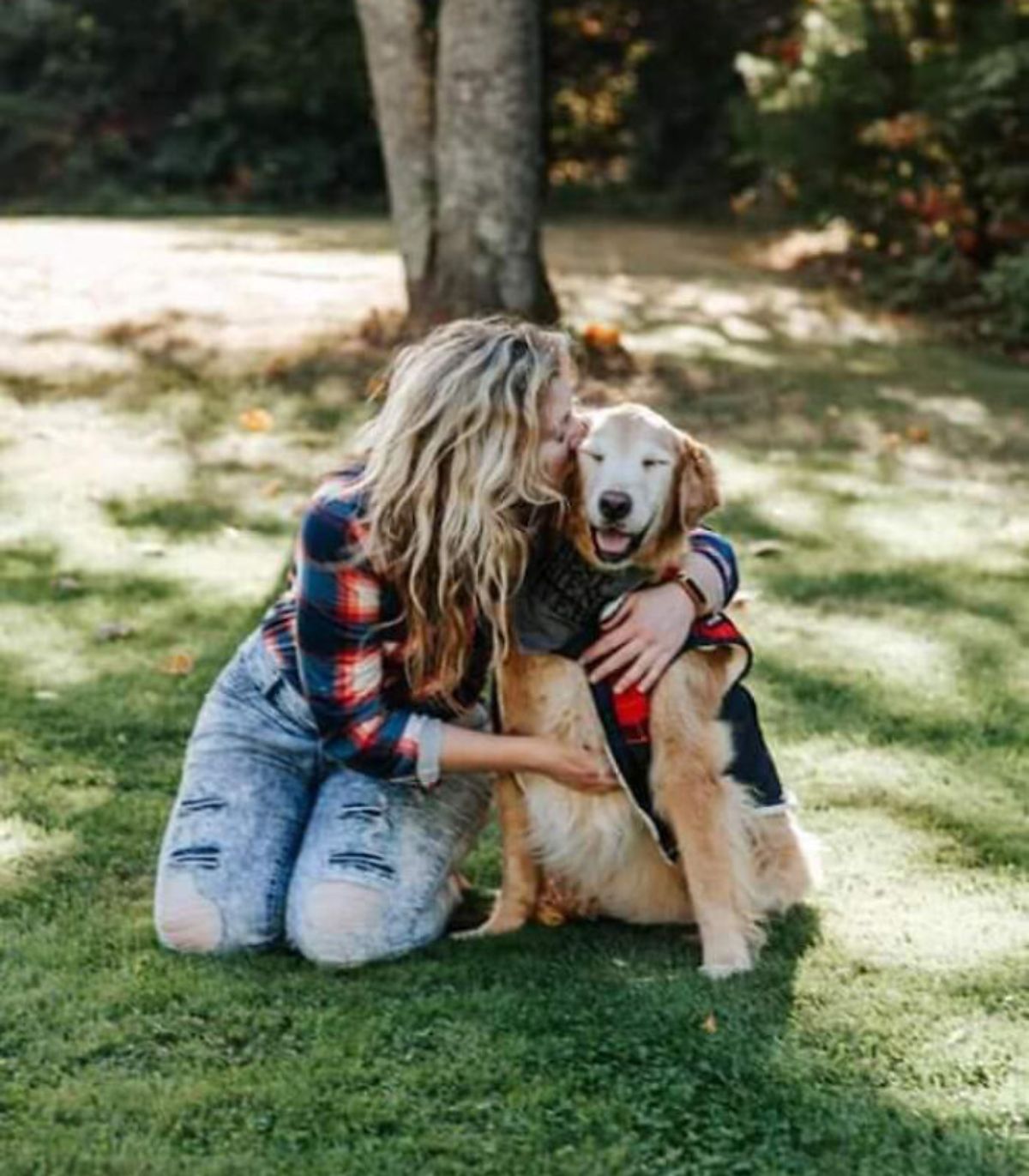 old smiling golden retriever being kissed by a woman