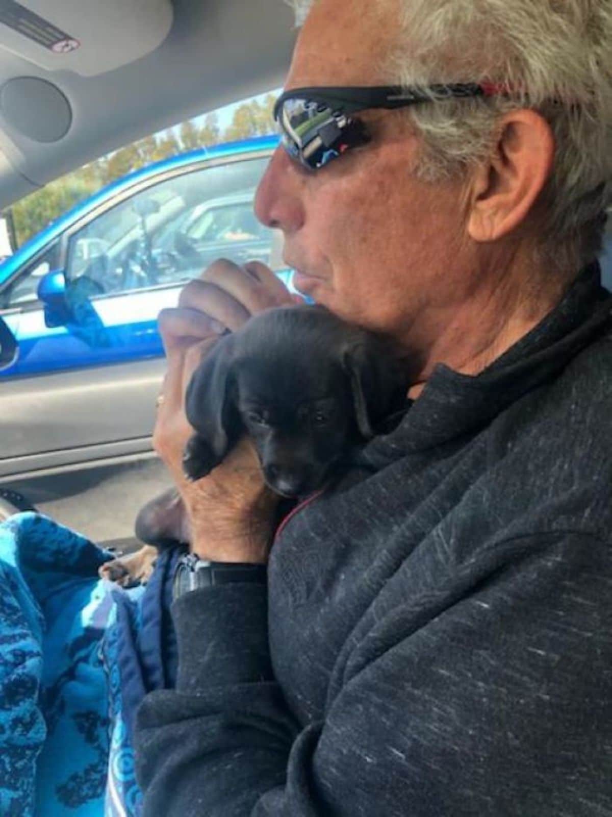 small black puppy being hugged by an old man in a vehicle