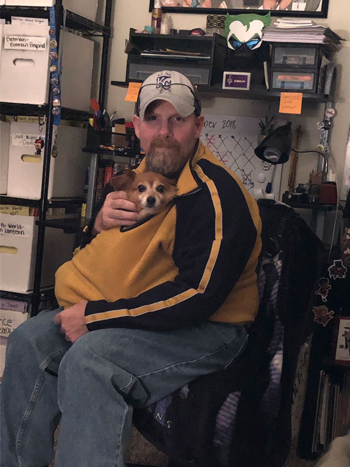 small brown and white dog inside a man's yellow and black sweatshirt and the dog is peeking out