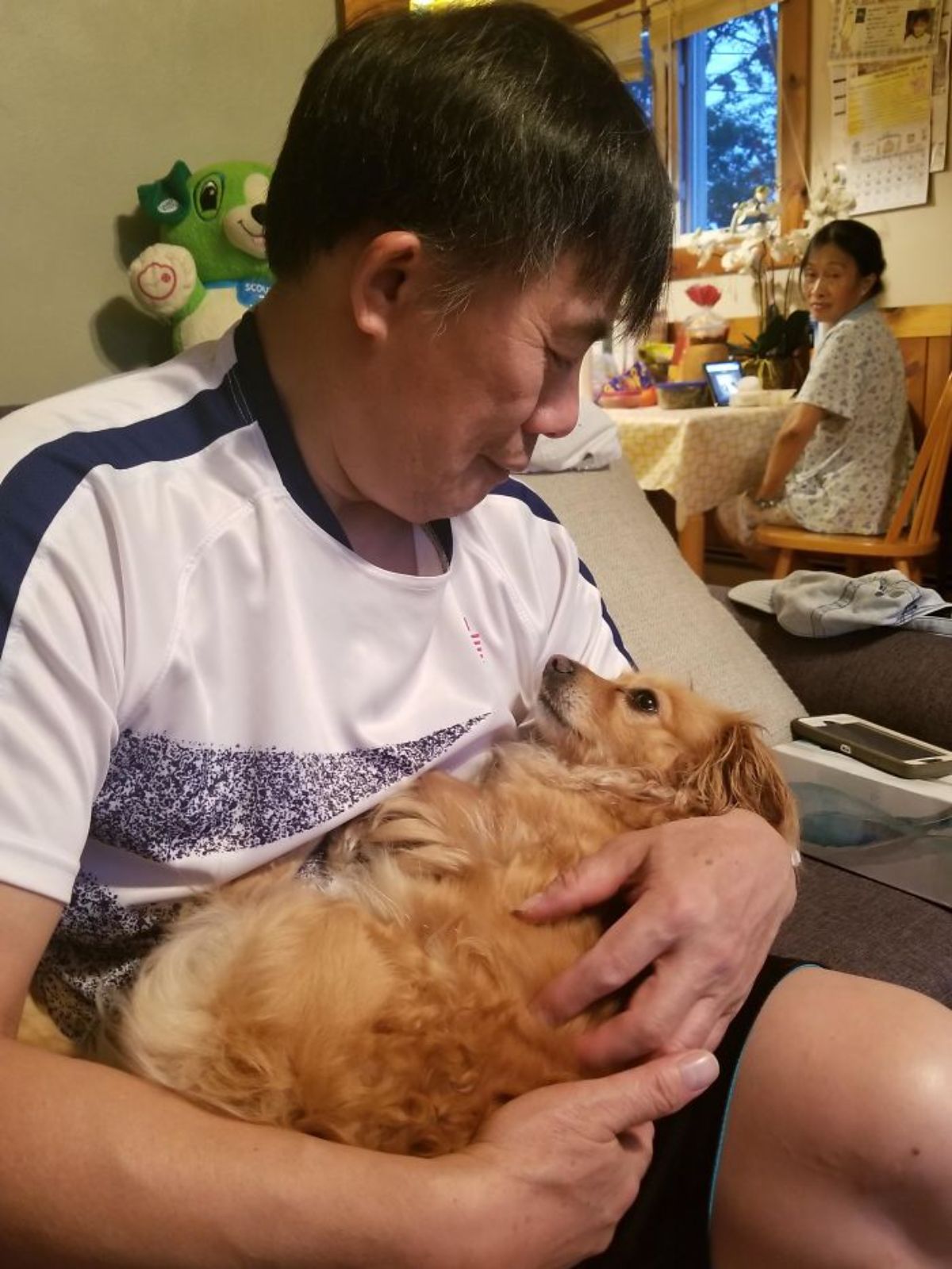 small fluffy brown dog being held like a baby by a seated old man