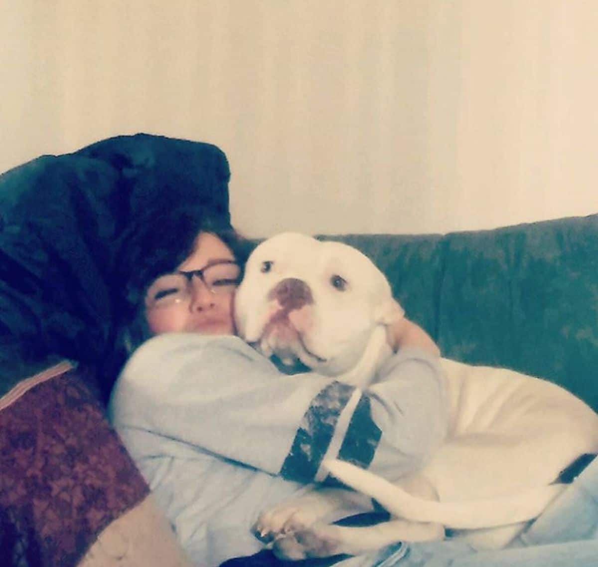 white pitbull laying on a girl and being hugged by her