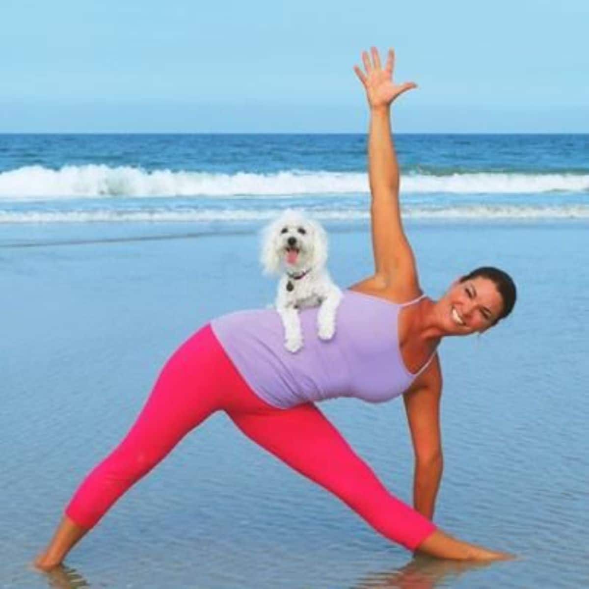 woman at a beach making an inverted simple h with a small white fluffy dog laying on her side