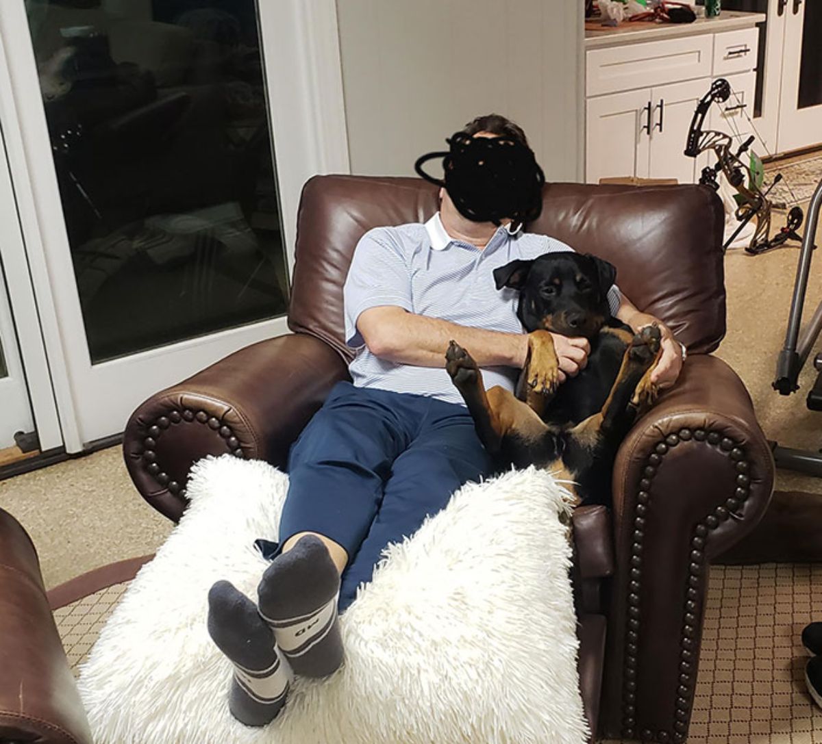 black and brown dog sitting on a brown chair cuddling with a man